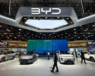 A large exhibition booth displays electric vehicles under a BYD logo, with visitors walking through the space