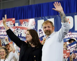 Graham Platner and wife Amy Gertner wave with raised arms at a campaign event