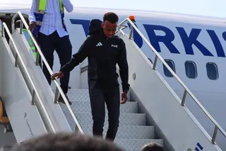 Omar Irfan, wearing a black Fifa hoodie and trousers, walks down the white metal stairs from the white Turkish Airlines plane