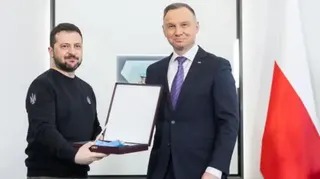NurPhoto via Getty Images A man with a beard holds a box containing a medal (L) while another man stands in a suit with a red and white flag to his right