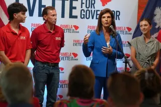 Lt. Gov. Pamela Evette speaks at a microphone, with three people in campaign shirts standing beside her