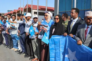 A crowd of people holding Somalia flags (pale blue with a white star) and pictures of Omar Artan