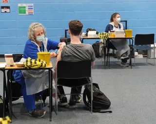 A student receives an injection of a vaccine from a nurse in a university sports hall
