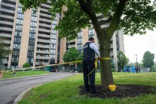 a police officer ties yellow crime scene tape to a tree