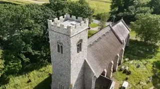 A church pictured from above, with a graveyard around and headstones. There are trees.