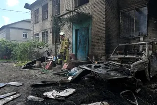 A Ukrainian rescuer stands on the porch of a damaged building.
