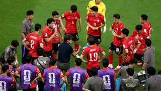 Myung-Bo Hong giving instructions to Korea Republic players during hydration break on soccer field.