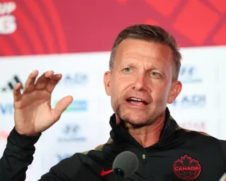 Jesse Marsch in a Canada jacket gestures with his hand while speaking at a press conference
