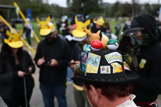 A player wearing a hat decorated with Pokemon characters and trading cards plays Pokemon GO on a smartphone during the in-person Pokemon GO Tour: Kalos Los Angeles 2026 event at the Rose Bowl Stadium in Pasadena, California, on February 20, 2026.