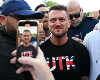 Tommy Robinson stands among a crowd as someone holds up a phone to photograph him
