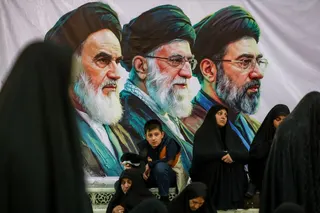 People gather near a banner with images of Iran's late leader of the Islamic revolution Ayatollah Ruhollah Khomeini, Iran's late Supreme Leader Ayatollah Ali Khamenei and Iran's Supreme Leader Mojtaba Khamenei.