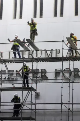 Reuters Workers stand on scaffolding in front of the sign and gesture