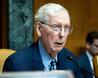 older man in blue suit speaks into microphone