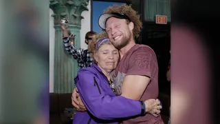 Daredevil Andy Lewis is wearing a black visor and maroon T-shirt as he has curly, light brown hair and a short beard in this photo, where he hugs his mother Lynn after setting a world record in Las Vegas