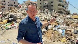 John Sudworth points towards rubble, the remains of a building, in Dahieh