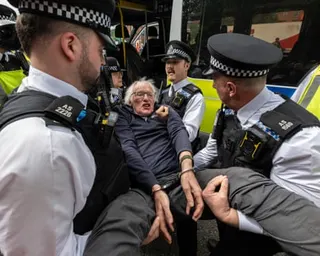 Police officers carry an older, handcuffed man into a police van