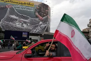 A man flashes a victory sign as he carries an Iranian flag in front of an anti-U.S. billboard depicting the American aircrafts into the Iranian armed forces fishing net with signs that read in Farsi: "The Strait of Hormuz will remain closed