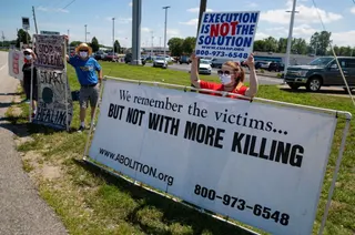 protesters hold signs against the death penalty outside of a federal execution facility