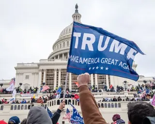 large group of people stand outside, some scaling a white dome building, while holding american flags and trump banners