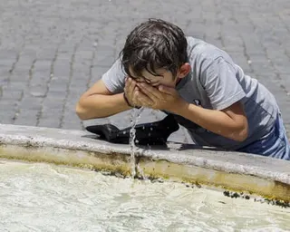 A young boy splashes water on his face from a fountain in Italy