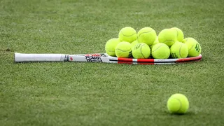 A tennis racket stacked with tennis balls on the grass at Aorangi Practice Courts.