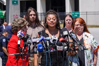 a woman speaks into a set of microphones while people stand behind her