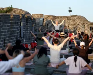 A yoga instructor leads a large group in a pose on the Great Wall of China at sunset