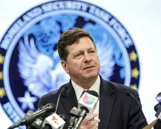 Man speaks at a press conference with multiple microphones and a blue seal backdrop