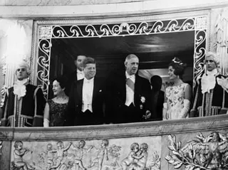 Yvonne de Gaulle, John F Kennedy, Charles de Gaulle and Jackie Kennedy on an ornate balcony, flanked by footmen