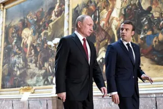 Vladimir Putin and Emmanuel Macron walk past very large paintings of historical battle scenes