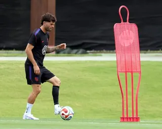 Christian Pulisic in black kit dribbles a ball near a tall pink training mannequin on a grass field