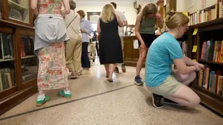 A black line across a floor in a library, people looking at books.