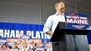 Platner speaks at a campaign rally podium with supporters cheering behind him