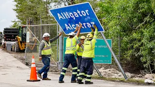 Workers install a permanent Alligator Alcatraz sign