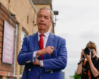 Nigel Farage stands outside a building as a woman takes a photograph of him.