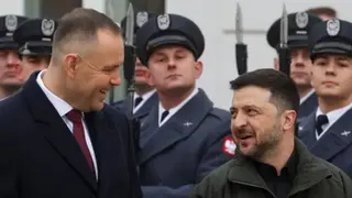 Reuters Polish President Karol Nawrocki and Ukrainian President Volodymyr Zelensky smile at each other while soldiers stand to attention behind them.