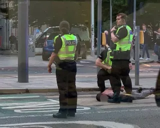 Two police officers in high-visibility vests stand over a person lying on the ground on a street