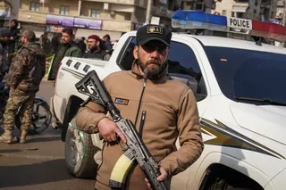 An armed member of the security forces stands in a street, holding a gun.