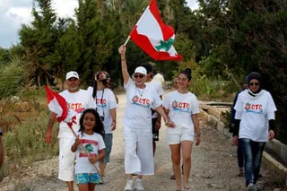 Mona Khalil waves a Lebanese flag as she walks with a group of people along a path