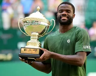 Frances Tiafoe in a green shirt holds the Halle Open trophy.