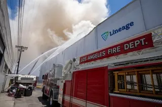 Fire department trucks spray water at a warehouse fire producing billowing smoke