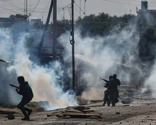 Armed officers crouch in a street filled with tear gas smoke amid scattered debris