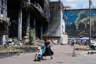 A mother pushes a stroller past a damaged building covered with street artist paintings and a big city marketplace that was destroyed recently by Russian missiles in Kyiv, Ukraine, Monday, June 22, 2026. (AP Photo/Efrem Lukatsky)