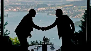 Two figures in silhouette shake hands with a lake visible behind them, at talks in Switzerland between the US and Iran