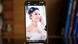 A posed image of a mobile phone stood vertically, displaying a scene from a Chinese micro drama involving a bride smiling as the groom strokes her face