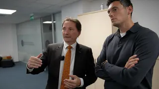 Dan Cimpean - standing explaining things to reporter Joe Tidy. Cimpean has brown hair and is wearing an orange tie