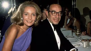 Barbara Walters and Alan Greenspan are photographed at a black tie dinner in 1977. They are looking at the camera and smiling. Waters is wearing a blue dress and Greenspan is wearing a tuxedo