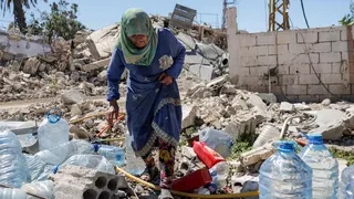 Khadija Amara fills a jerrycan with water as she sits among the rubble of a house, which was damaged by an Israeli strike, in Qlaileh in the Tyre district, southern Lebanon
