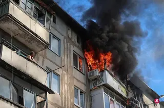 乌克兰东部顿涅茨克州德鲁日基夫卡一栋住宅楼遭俄罗斯无人机击中后起火，附近居民站在阳台上查看火势。 （路透社）