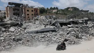 A man riding a motorcycle past destroyed buildings in the village of Mayfadoun, southern Lebanon (23 June 2026)